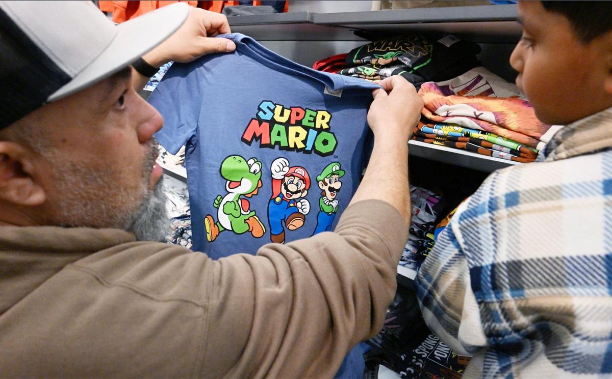 El coordinador del proyecto Live Again Fresno, Leonard Medina (izquierda), ayuda a un niño a elegir camisetas durante una compra en Old Navy, el lunes 18 de diciembre de 2023 por la mañana, en Fresno.