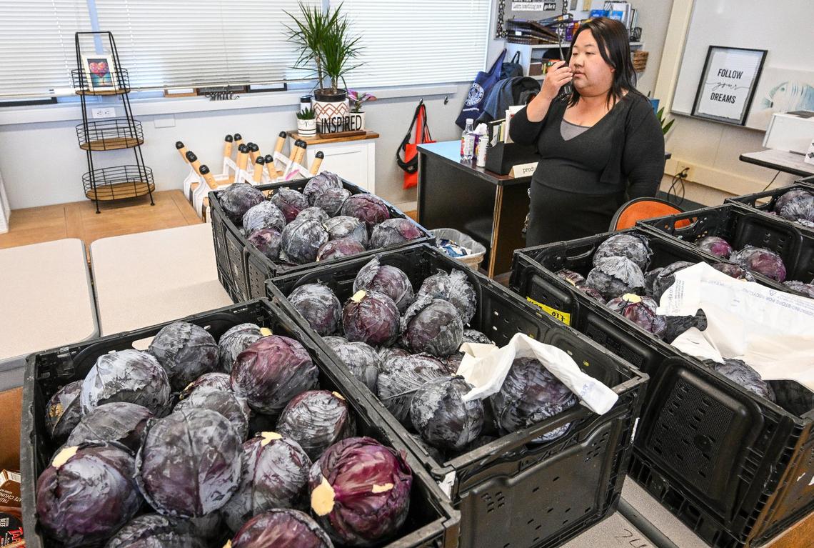Fort Miller Middle School Community School coordinator Xee Xiong radios the office while standing in front of bins of donated cabbages during the Fresno school’s Food Pantry & Clothing Closet event at the Fresno school on Friday, March 8, 2024.