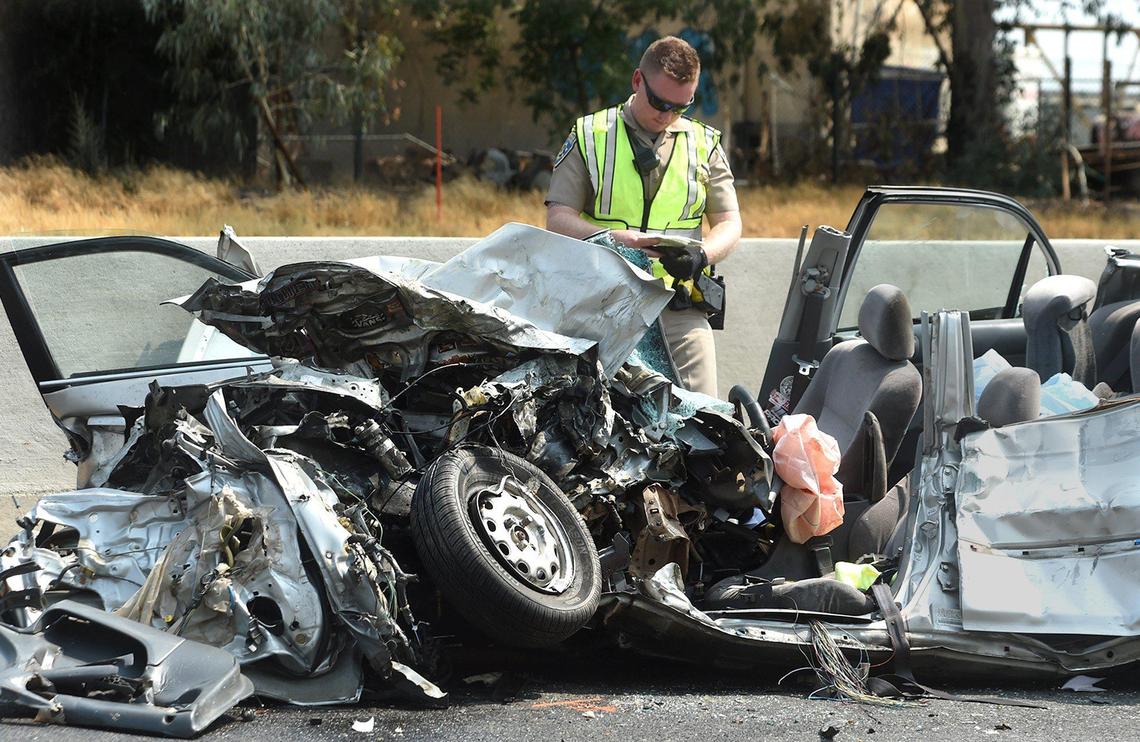 A CHP officer conducts his investigation at a crumpled Honda Civic which ran into the back of a Caltrans truck involved in median clean up work on freeway 99, south of Ashlan Ave., Saturday morning, Aug. 14, 2021.