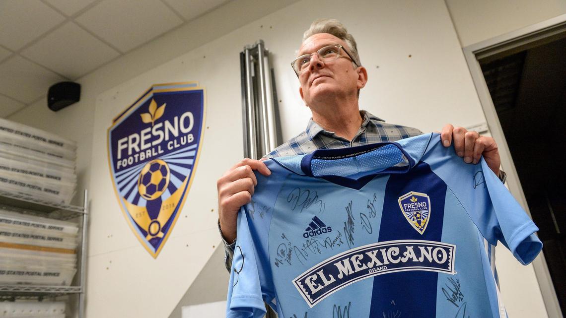 AlphaGraphics owner Dean Titus holds up a Fresno FC jersey signed by team members at his central Fresno print shop on Tuesday, Jan. 8, 2020. Titus said he enjoyed a good business relationship with the Foxes until the soccer team relocated leaving behind a stack of unpaid invoices totaling more than $5,000.