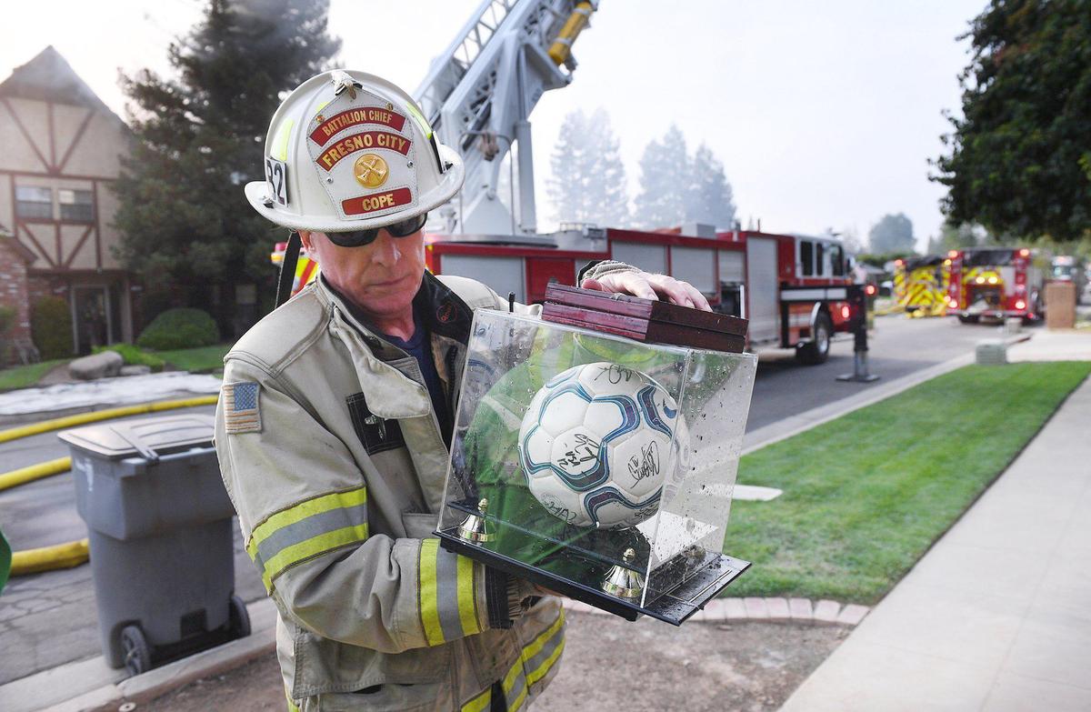 Fresno Fire Department Battalion Chief Thomas Cope carries an autographed soccer ball from one of two homes destroyed by flames Monday, July 26, 2021, in northwest Fresno, California. The ball is signed by Chad McCarty, captain of the Team USA squad that played in the 2000 Sydney Olympics, and was one of many items firefighters helped salvage and move to a neighbor’s garage across the street.