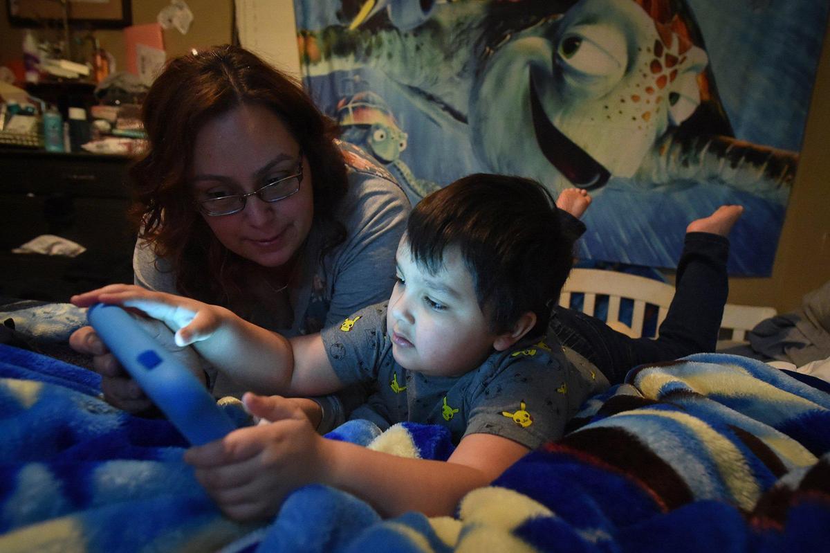Nicole Miller works with her son, 4-year-old Immanuel Grijalva- the only one of her seven children not yet in school, on his tablet device, Jan. 25, 2021. The family is struggling with internet issues as they study at home during the pandemic.