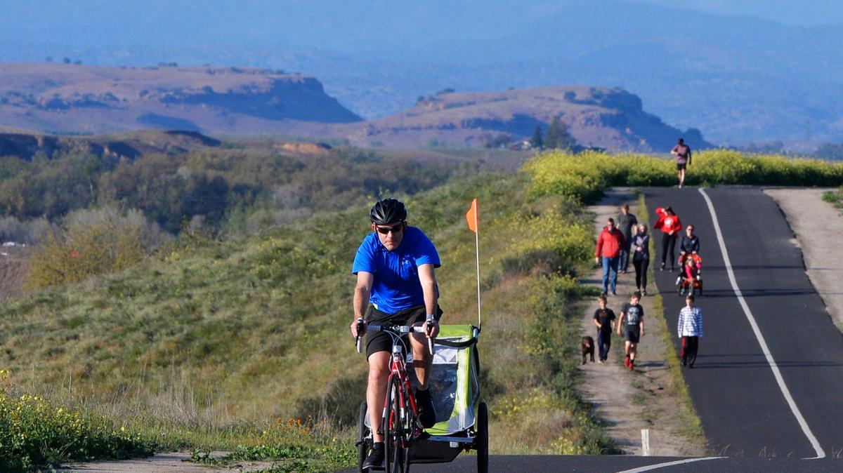 Fresno’s Mike Gallagher, left, rides pulling a trailer along the Lewis S. Eaton Trail during a break in a storm last spring. The trail runs to and through Woodward Park.