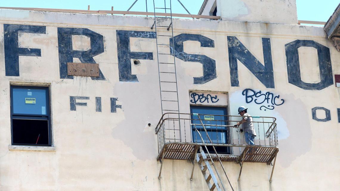 A window installer on a fire escape balcony, works on the final fitting of a 7th floor apartment window of the historic Hotel Fresno, which is undergoing renovation into a 79-unit affordable housing complex, Wednesday July 15, 2020. The work has been slowed by the pandemic in that fewer workers are allowed on site at one time.