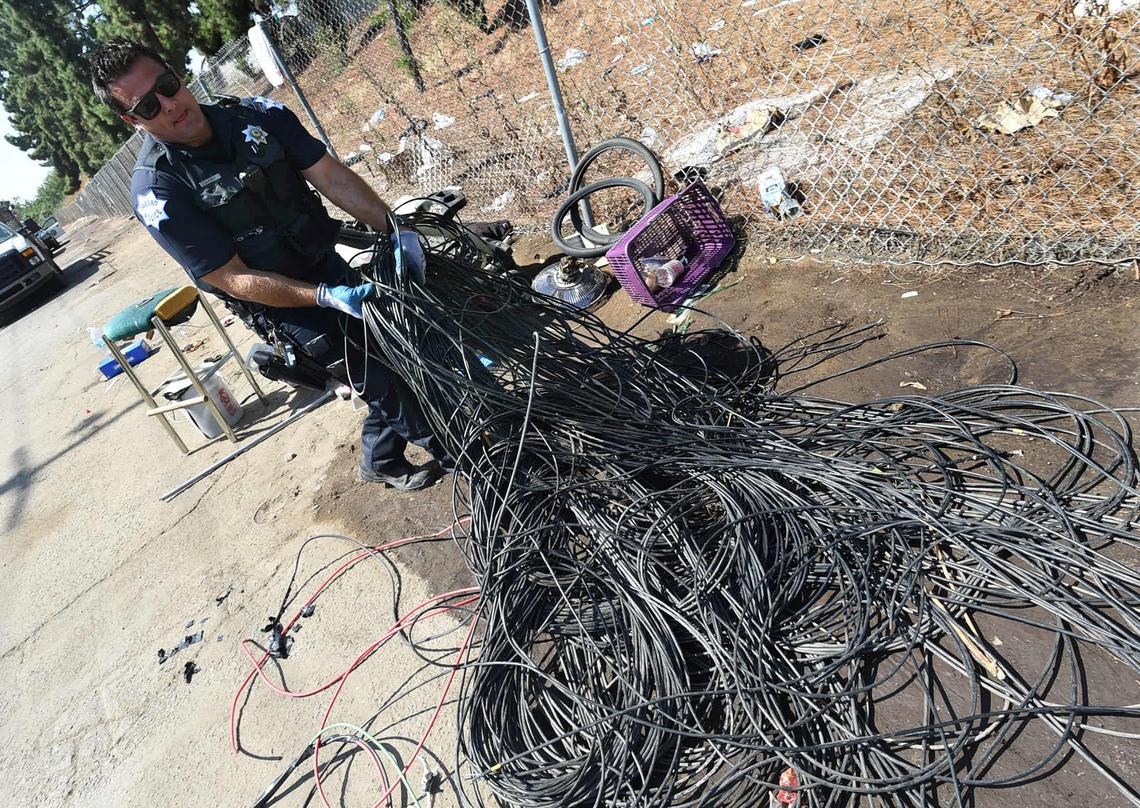 Fresno Police Officer Noel Perez gathers electrical wiring (commonly stolen for its recycling value) to be put in a waiting garbage truck for later sorting during a cleanup of an alley near Highway 41 on Wednesday morning, Aug. 14, 2018.