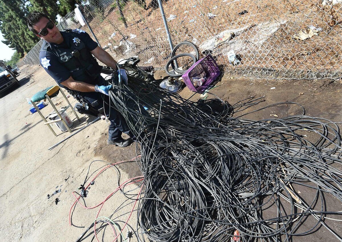 Fresno Police Officer Noel Perez gathers electrical wiring (commonly stolen for its recycling value) to be put in a waiting garbage truck for later sorting during a cleanup of an alley near Highway 41 on Wednesday morning, Aug. 14, 2018.