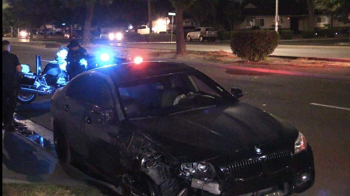 A black BMW sedan sits on the roadway on Bullard Avenue after a hit-and-run collision in Fresno, California that sent a woman in a gray Kia sedan to the hospital.