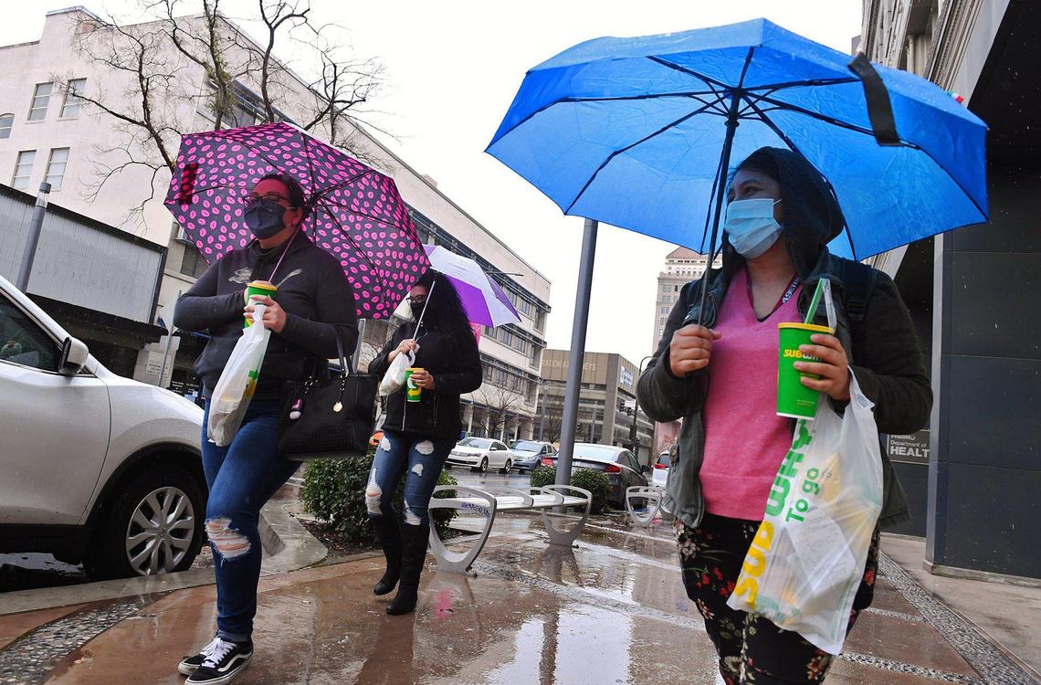 IRS employees Elena Oceguera, left, Maria Lopez, center background, and Monica Castillo, right, return to work following lunch as rain continues to fall along Fulton Street Thursday, Jan. 28, 2021 in downtown Fresno.