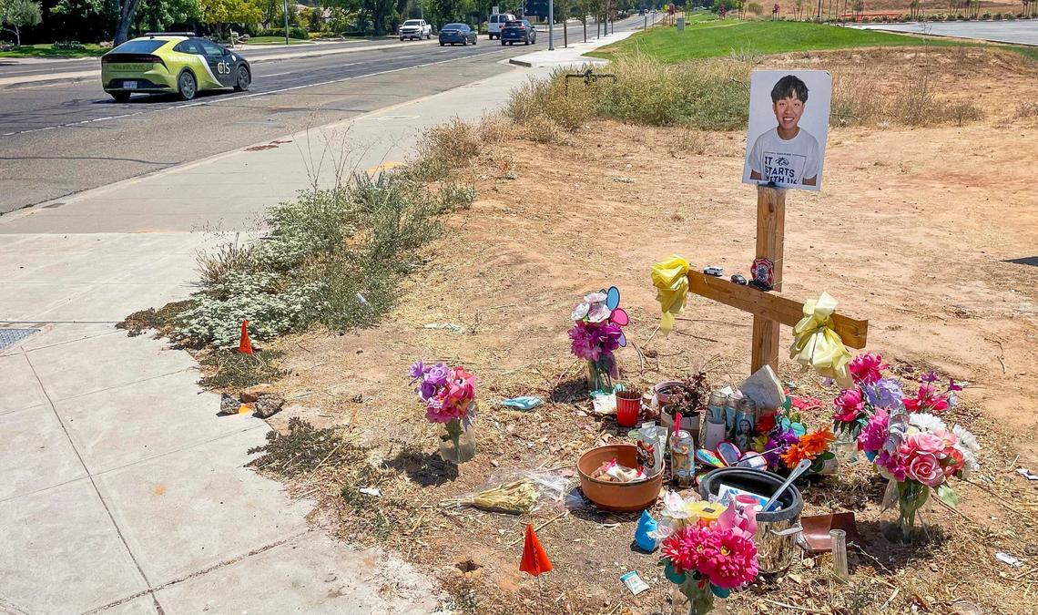 Cars turn past a memorial to the victim of a fatal crash at the intersection of Audubon and Friant Monday, Aug. 5, 2024. Several safety measures have been implemented along a dangerous section of Friant Road in north Fresno including high-visibility crosswalks, reflective signal backplates, and no right turn on red signs.
