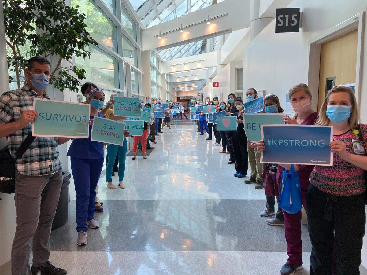 Health professionals inside Kaiser Permanente Fresno hold signs to celebrate Ronald Hill’s discharge from the hospital in May after recovering from COVID-19.