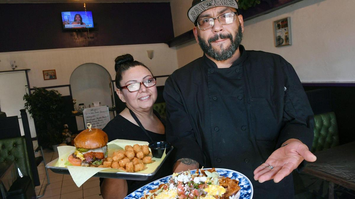El propietario y chef Marcial González, a la derecha, sosteniendo un plato de chilaquiles, posa con su esposa Michelle González, a la izquierda, sosteniendo su hamburguesa West Side. Abrieron Grandma Jane's Kitchen, un nuevo restaurante en E Street, cerca del Chinatown en el centro de Fresno. Fotografiados el martes 11 de octubre de 2022.