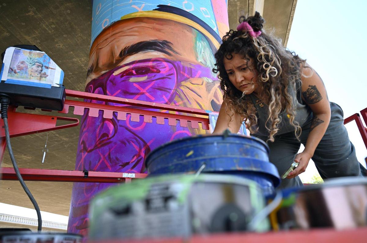 Muralist Andrea Cano Torres adds more paint to a brush as she works on a mural featuring US poet laureate and writer Juan Felipe Herrera underneath Highway 180 at San Pablo Park Thursday, July 17, 2025 in Fresno. The murals by several artists are a collabortion between the Fresno Arts Council and Caltrans, said muralist ANdrea Cano Torres.