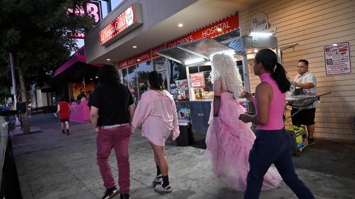 Peatones pasan junto a Jaime Gómez, un vendedor de comida que vende hot dogs en la acera de Olive Avenue, en el Distrito Tower en Fresno, la noche del miércoles 19 de julio de 2023.