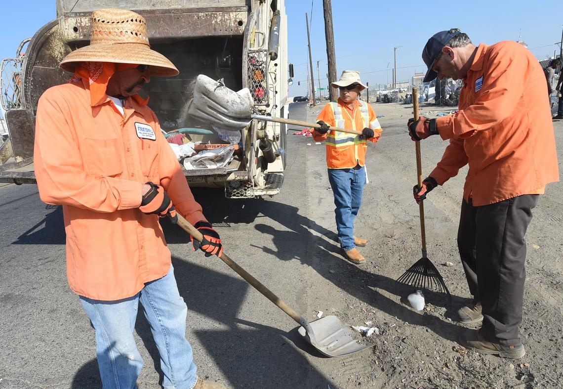 Fresno city sanitation workers from left, Chris Quinonez, Ray Velasquez and Gary Bowin, scoop up the last bit of debris - a hypodermic needle was found among the trash - during a cleanup of G Street near Ventura Street on Wednesday morning, Aug. 14, 2018.