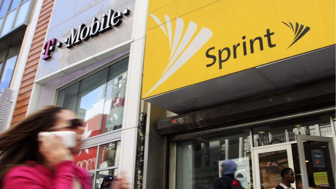 A woman using a cell phone walks past T-Mobile and Sprint stores, Tuesday, April 27, 2010, in New York.