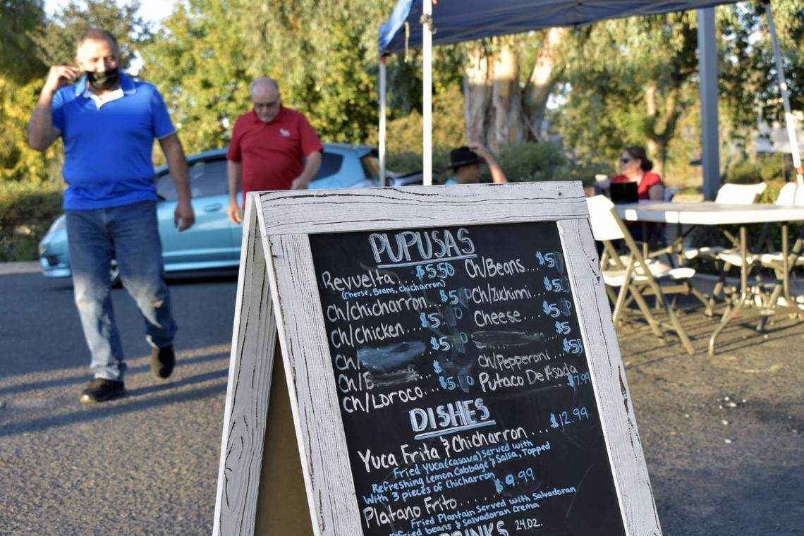 Adonay Díaz, con mascarilla, camina con un cliente hasta el menú de ‘Plátano, Pupusas Y Cafecito’ el 7 de octubre. Adonay Díaz dijo que la decisión de su familia de venir a Estados Unidos se dio después de que él ya había luchado en la Guerra Civil salvadoreña y estaba a punto de entrar en una segunda campaña.