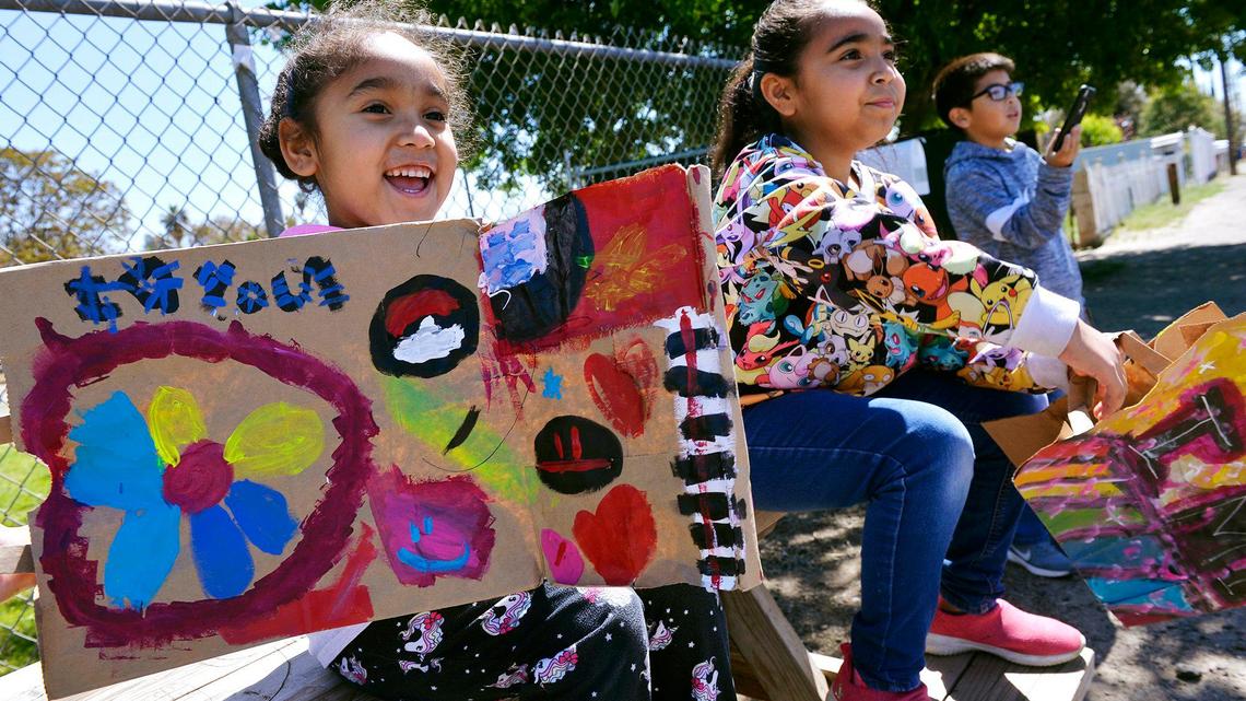 Alana Silos, 6, left, with Alexiyaah Silos, 9, middle, and Isiah Tamez Silos, 9, far right, wait for West Park Elementary staff’s drive-by parade to pass as staff wish their home-bound students well Thursday, April 2, 2020, in West Park, southwest of Fresno.