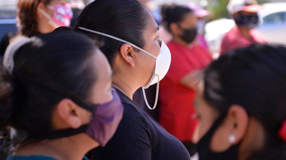 Masked farmworker families stand waiting May 9, 2020 near Rolinda, CA.