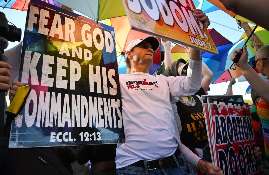Two members of a group representing Westboro Baptist Church, center, are surrouded by Pride-themed umbrellas used as symbolic shields by a coalition of LGBTQ+ organizations and supporters in a counter-protest outside Roosevelt Hgh School Monday, Oct. 28, 2024, Fresno.