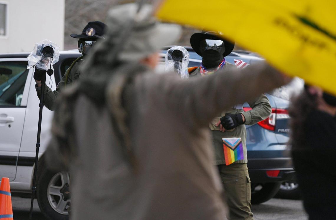 Two men claiming they are media stand with reflective glasses and cameras as a protester holding a yellow Do Not Tread On My flag paces at the end of a driveway at Our Saviour’s Lutheran Church while the Fresno Drag Fest is held inside Saturday, Dec. 10, 2022 in Fresno.