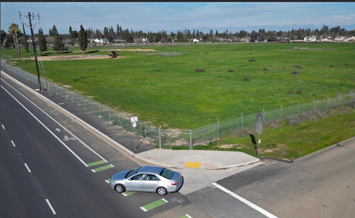 A car makes a turn from Geary Street onto Peach Avenue where a new 49-acre park, background, is being developed. Photographed Wednesday, Feb. 19, 2025, in Fresno.