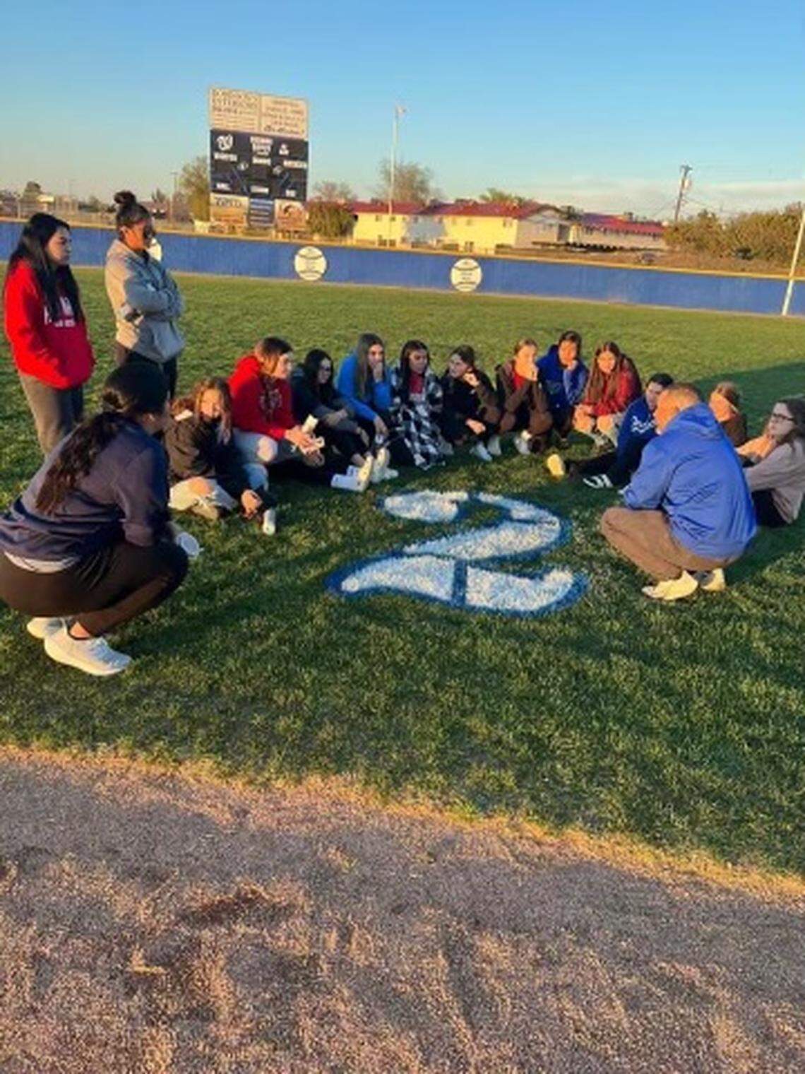 Hanford West players sit on the field around the No. 2 in memory of Marissa Cardona who was killed in a car crash on Saturday, March 5, 2022.