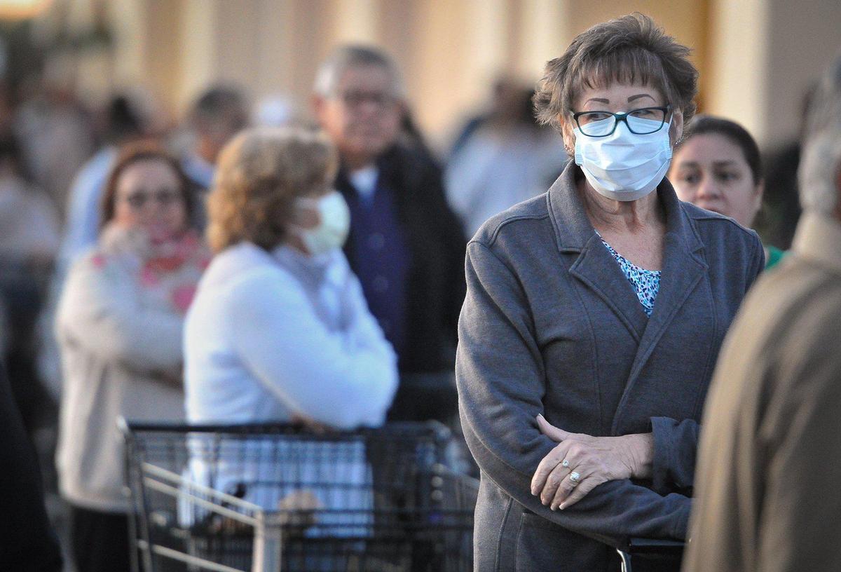 A woman in a protective mask waits in line at the Vallarta Supermarkets near Clinton Avenue and Highway 99 in Fresno with hundreds of others early Wednesday, March 18, 2020, amidst the coronavirus crisis.