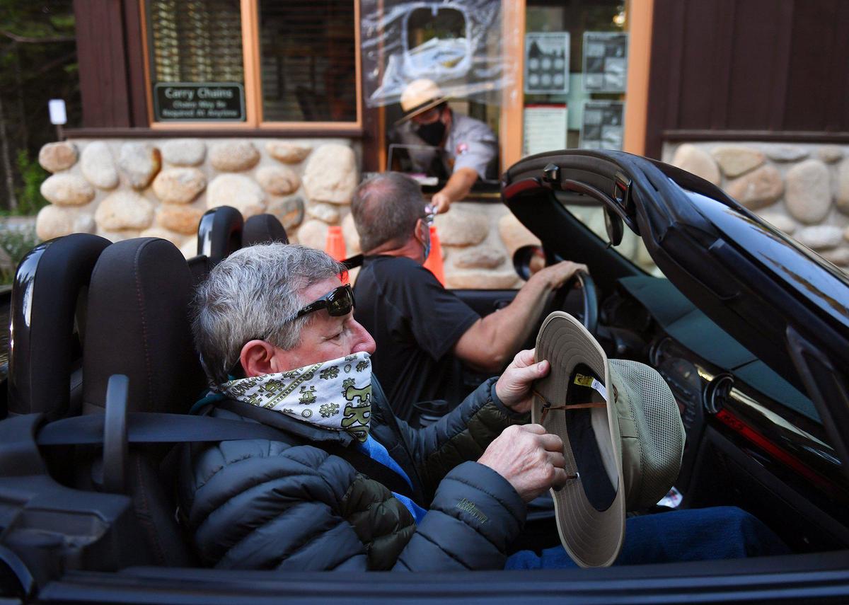 Richard Trotter, foreground, fixes his hat as a ranger hands his son Chad Trotter information at the south entrance of Yosemite National Park as it re-opens after a historic closure Thursday, June 11, 2020. The Trotters said they drove 12 hours from Prescott, AZ. just for the event.
