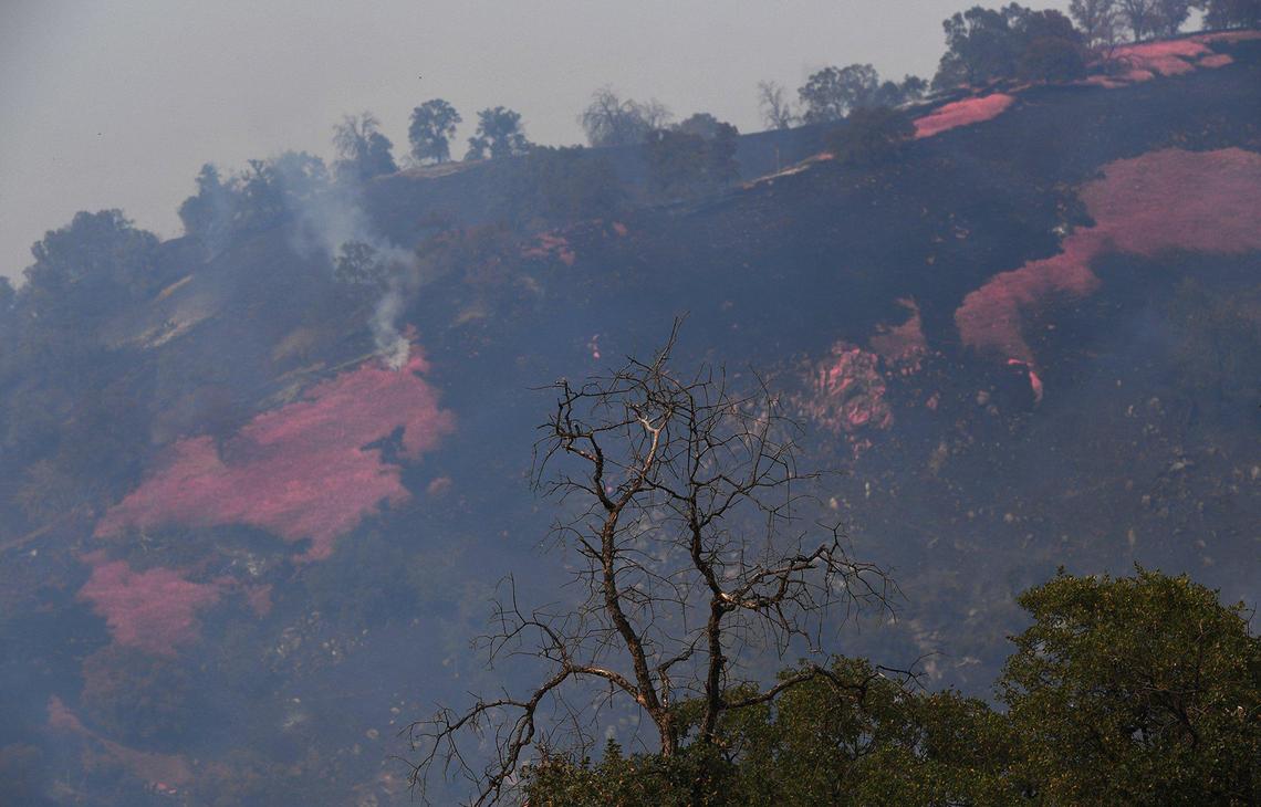 A distant hill smolders after fire retardant drops as the River Fire increases to 9,000 acres with 10% containment Monday, July 12, 2021, near Coarsegold.