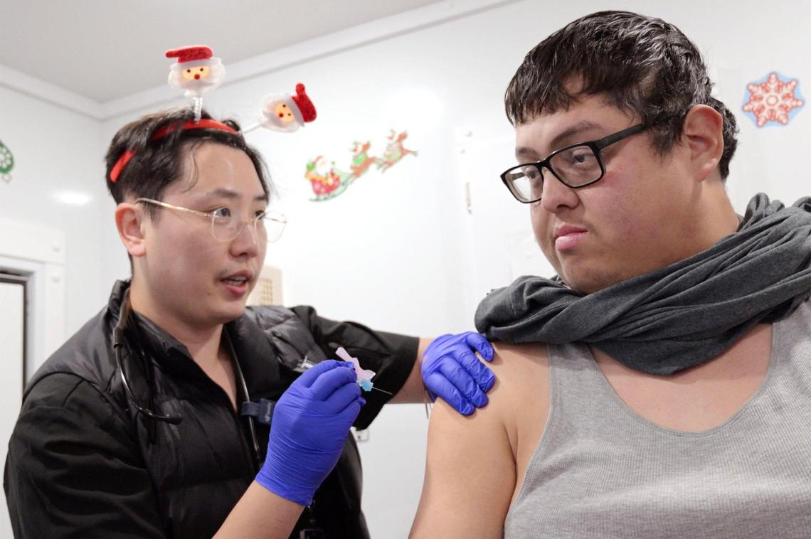 Medical Resident Sean Kim, DO, left, prepares to administer a COVID-19 booster shot to Mendota’s Kevin Arias-Romero, right, in the Saint Agnes Mobile Health Unit van during a Covered California event held in Mendota Thursday, Dec. 12, 2024.