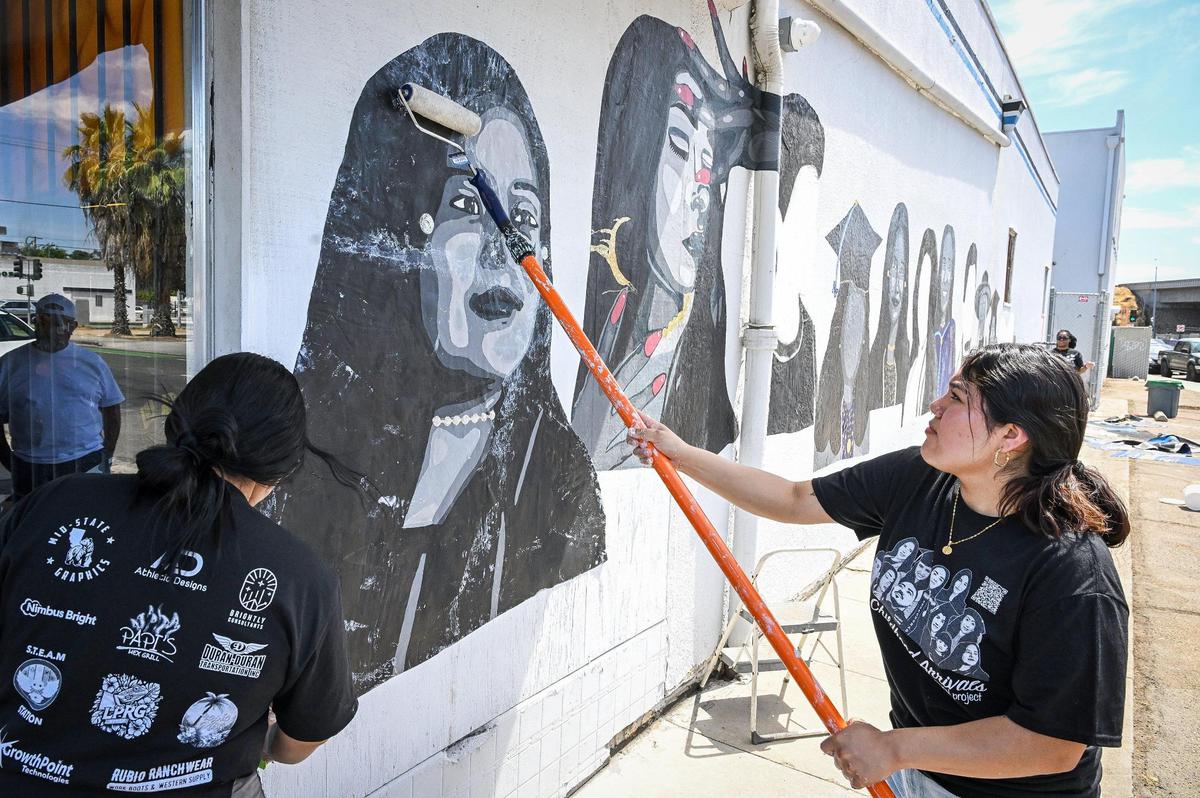 Muralist Michelle Cruz uses a paint roller to affix a mural print to the wall of the Fulton Studios building at Fulton and the 180 freeway in Fresno on Saturday, June 14, 2025.