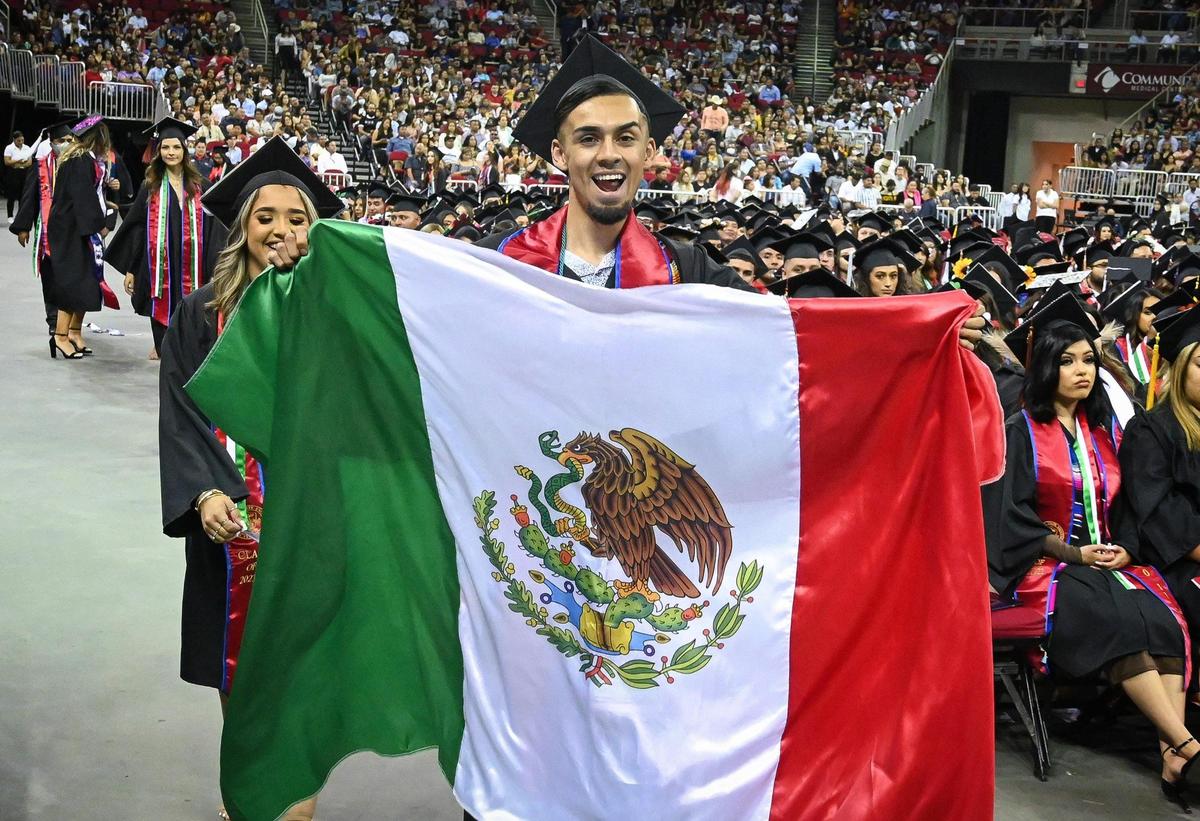 Graduate Joseph Espinoza waves a Mexican flag after walking across the stage to earn his degree during the 46th annual Fresno State Chicano/Latino Commencement Ceremony held at the Save Mart Center on Saturday, May 21, 2022.