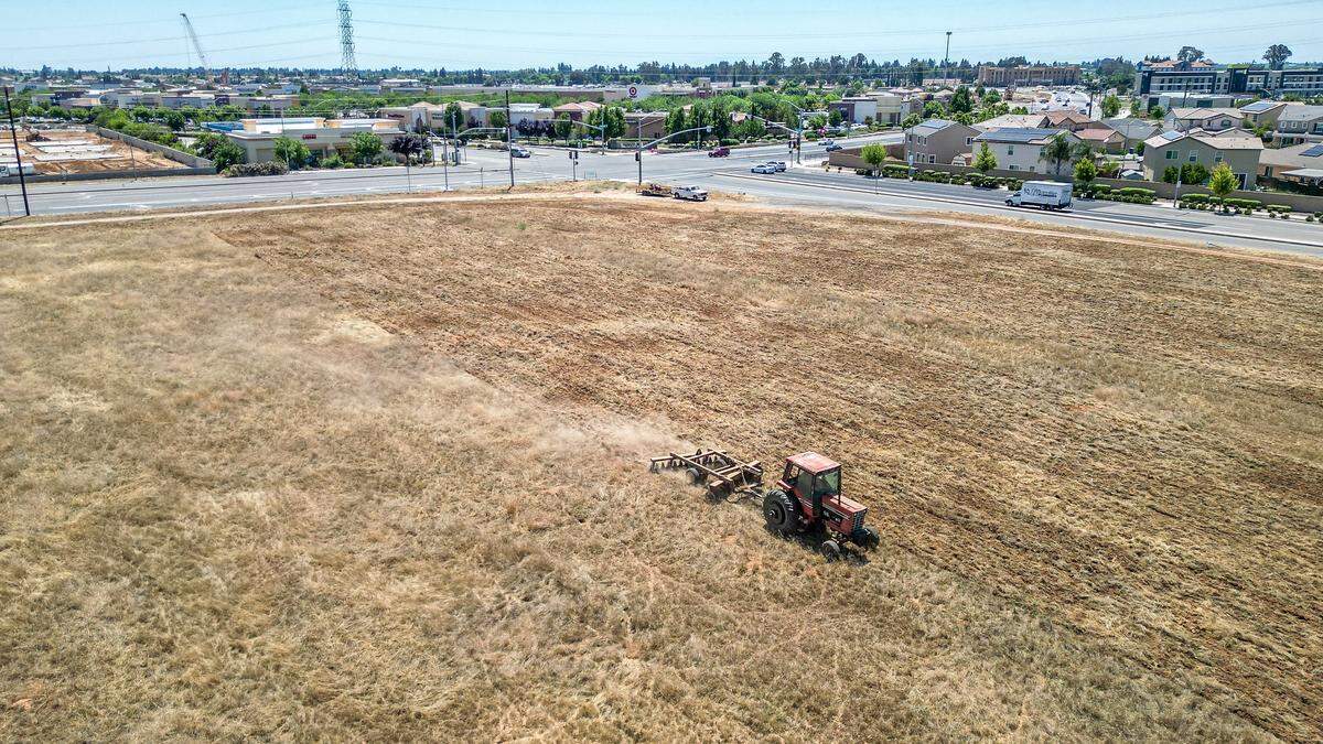 A tractor works in a large empty lot across from businesses in the Marketplace at El Paseo shopping center in northwest Fresno. The lot has been designated to be Fresno's largest Costco but zoning and environmental analysis setbacks have delayed the project.