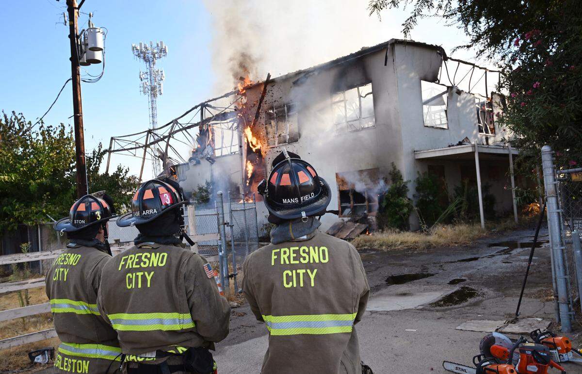 Firefighters stand by as a portion of a wall falls at the former Fresno County Coroner’s building burning Tuesday morning, Sept. 24, 2024 in Fresno.