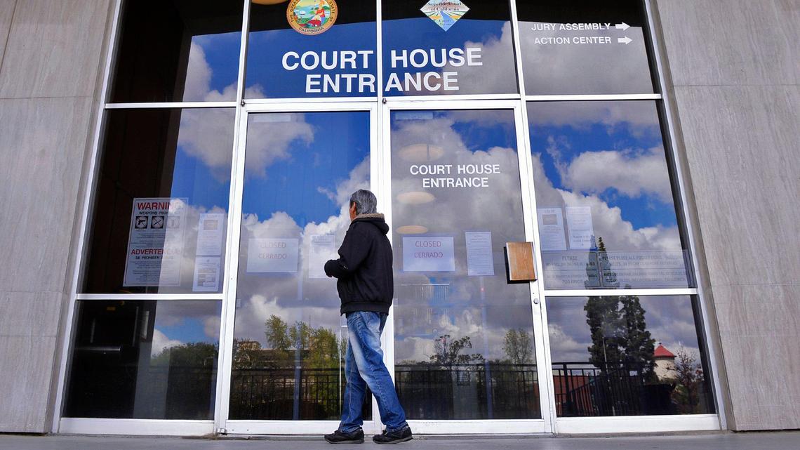 A man reads the notice on the front doors of the Fresno County Courthouse showing closure of the courts except for rare instances due to the coronavirus on Monday afternoon, March 23, 2020 in Fresno.