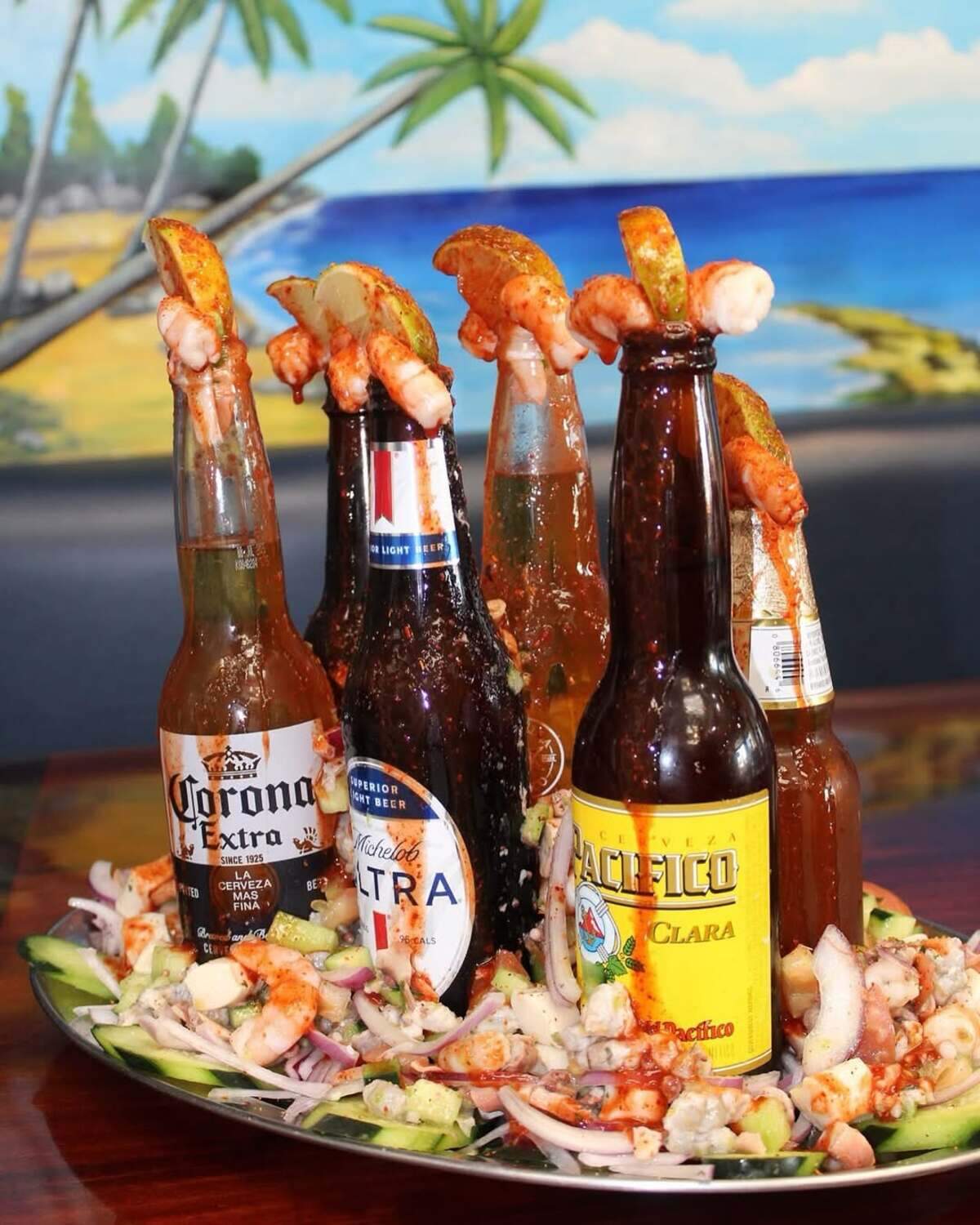 Some of their alcoholic drinks come at Mariscos El Barba Negra come in a bright, orange-reddish color, like the micheladas, the cervezas preparada. and a bottle of Corona drizzled with red chamoy with a shrimp on top.