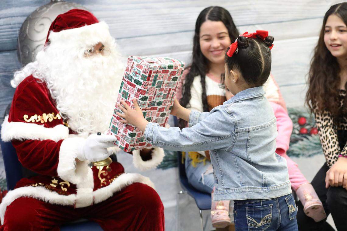 La niña de kindergarten Damaris Ayala, de 5 años, recibe un regalo de Santa durante el evento navideño de la Familia Migrante 2023 que se llevó a cabo en la biblioteca de la Firebaugh High School el 13 de diciembre.