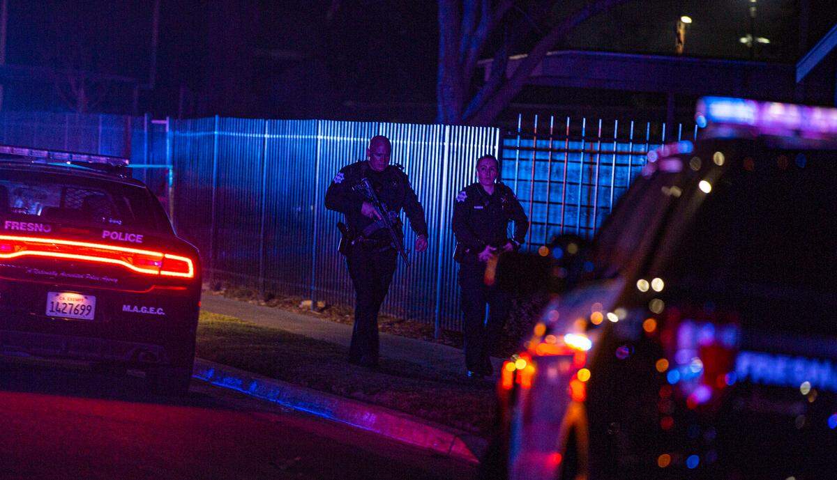 Officers walked the perimeter of a crime scene where two men were killed and two others were wounded in a shooting that at an apartment complex in southwest Fresno, on Sunday, Feb. 6, 2022.