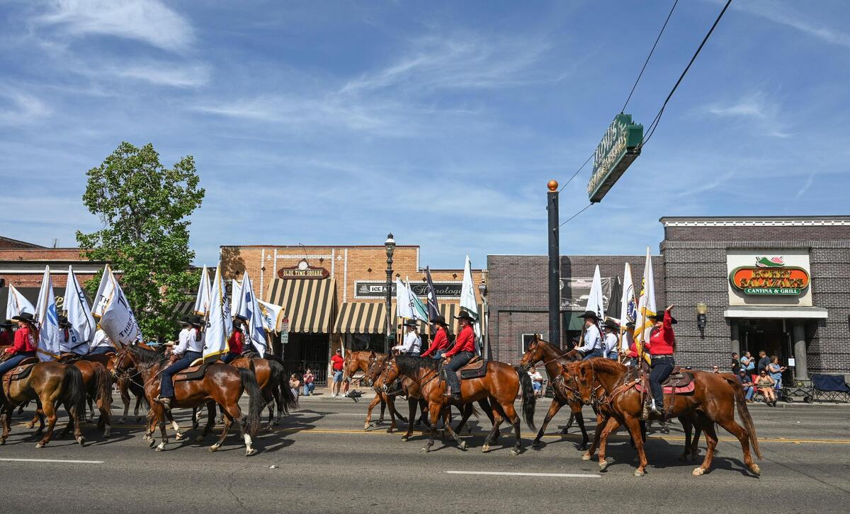 Parade participants mounted on horses hold sponsor flags as they head down Clovis Avenue during the 109th annual Clovis Rodeo Parade on Saturday, April 29, 2023.