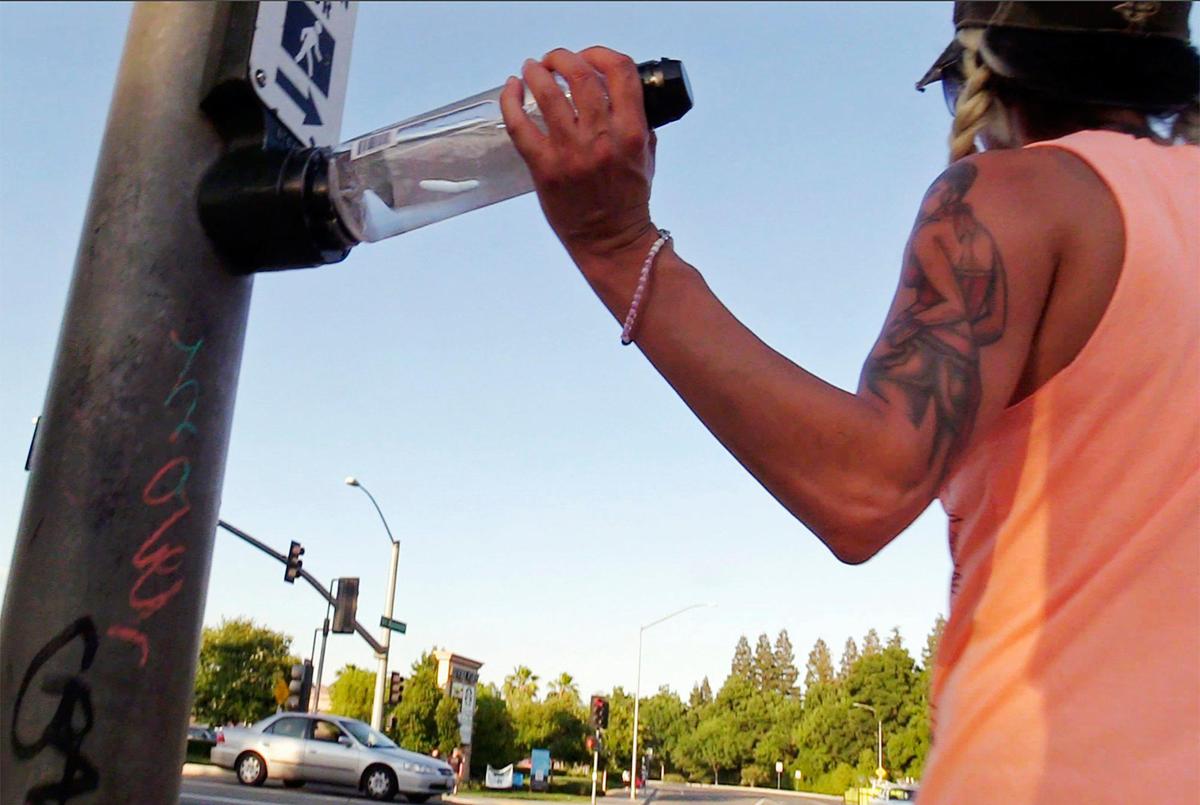 A runner uses her waterbottle to activate the “beg button” at Friant Rd. and Fort Washington Rd. Wednesday, June 3, 2020 in Fresno.