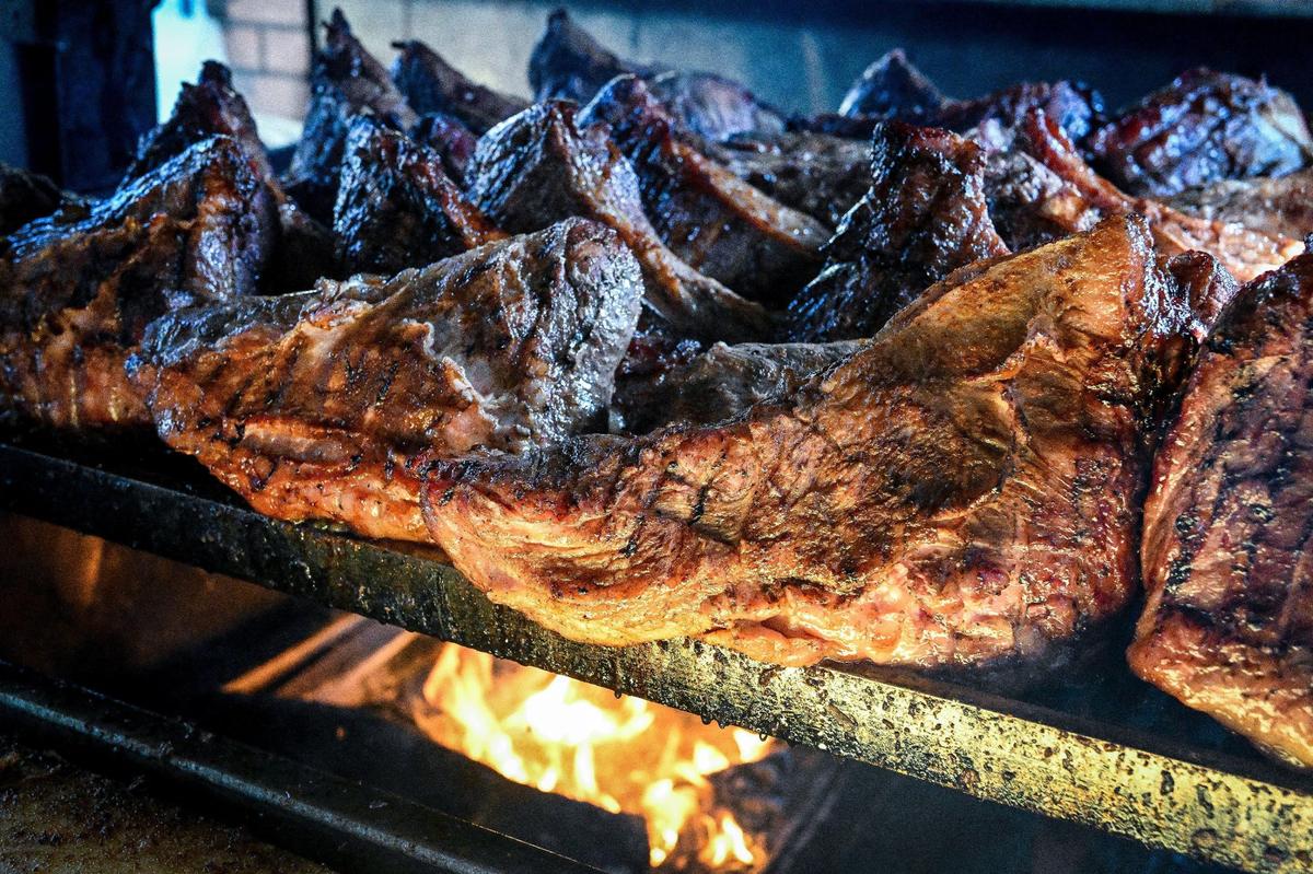 Tri-tip is pictured atop a grill with an open flame after smoking in a smoker for hours at Dog House Grill in Fresno on Aug. 6, 2024. The popular barbecue place cooks between 400 and 700 cuts of tri-tip every day.