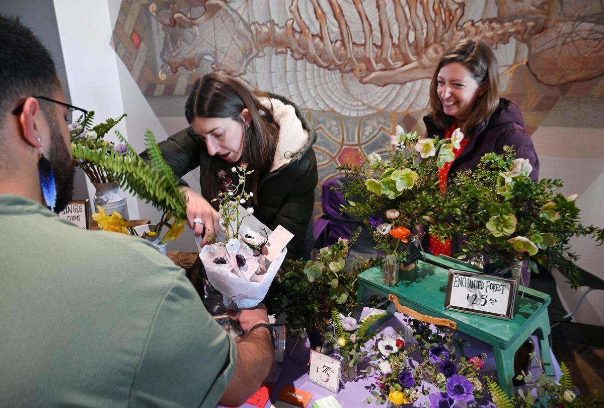 hannaH Poitras of hannaH Honey’s Flowers, left, and Mattie Avila, right, sell a bouquet of lowers to a customer at the first Flower Market, held inside the Sun Stereo Warehouse in downtown Fresno’s Brewery District Saturday, March 18, 2023.
