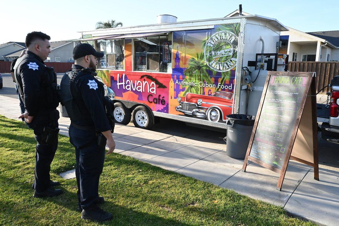 Two Fresno Police officers look at the menu for Lazaro and his wife Niermin Saldana’s new food truck Havana Cafe at a community park event Wednesday, March 16, 2022 in Fresno. Lazaro and Niermin Santana have opened a food truck staffed by family members which specializes in the Cuban food and coffee Lazaro remembers growing up with as a child.