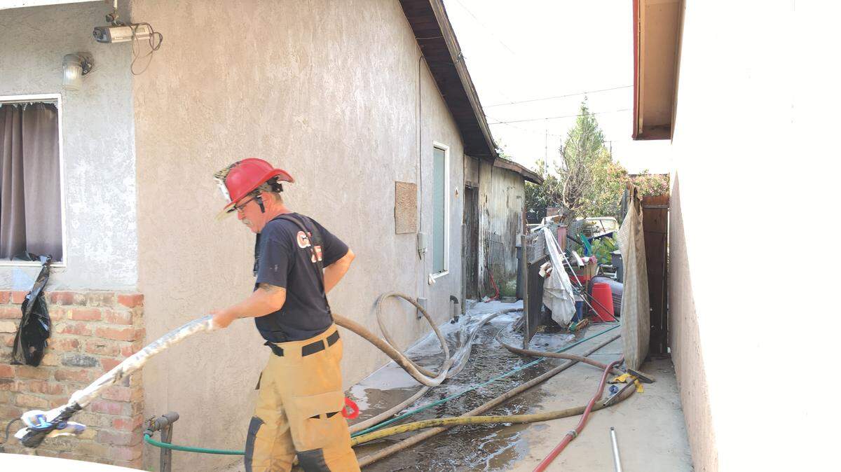 A Fresno firefighter drags a water hose Saturday, July 21, 2018 following a house fire operation in southeast Fresno. Fire battalion chiefs believe the fire is suspicious.