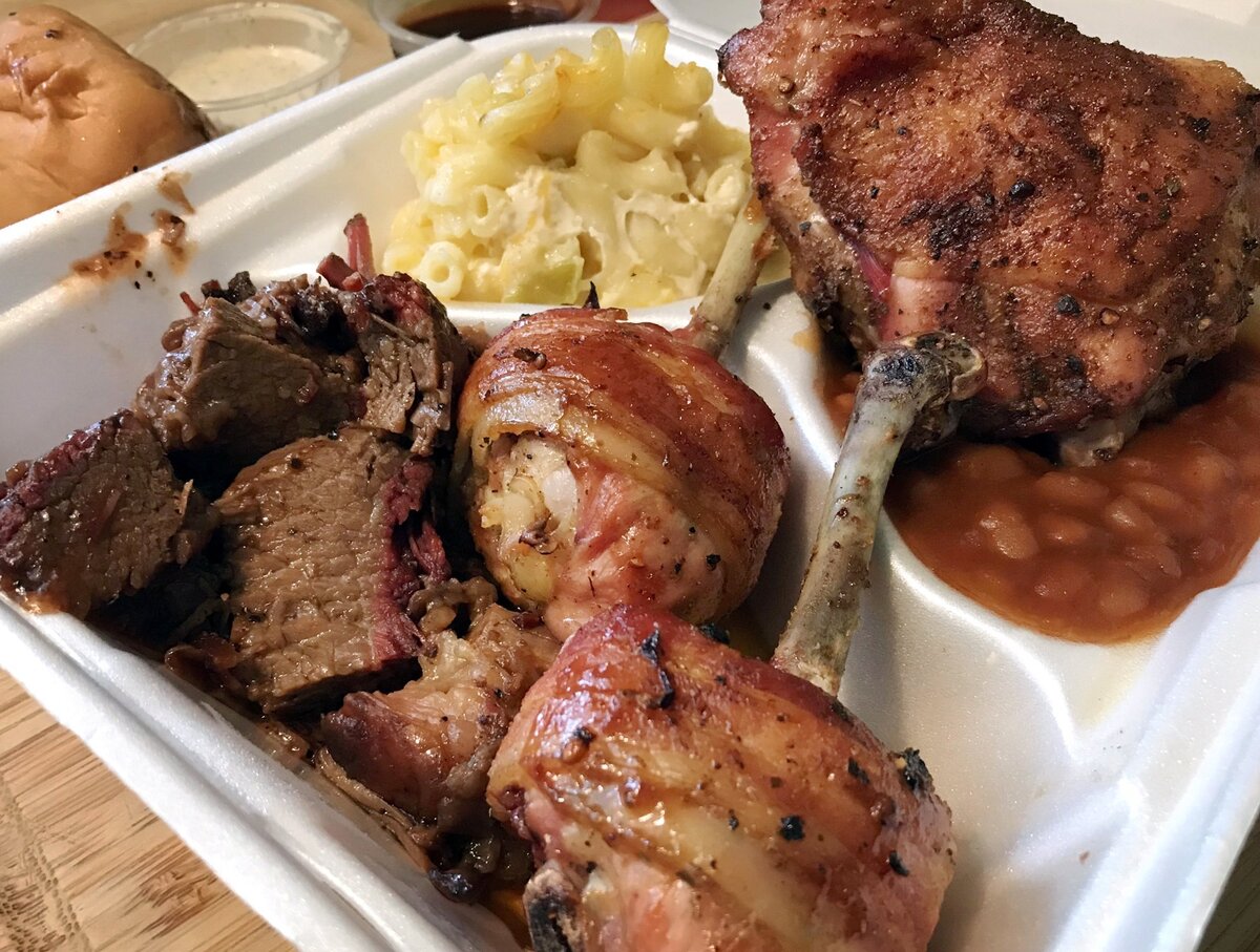 Bacon-wrapped chicken lollipops, center, with beef brisket, left, and a chicken thigh top right,, served with green chili mac-n-cheese and beans, from Mega Texas Barbeque, located in an Arco gas station at McKinley Avenue and Fresno Street. Photographed Jan. 24, 2019 in Fresno.