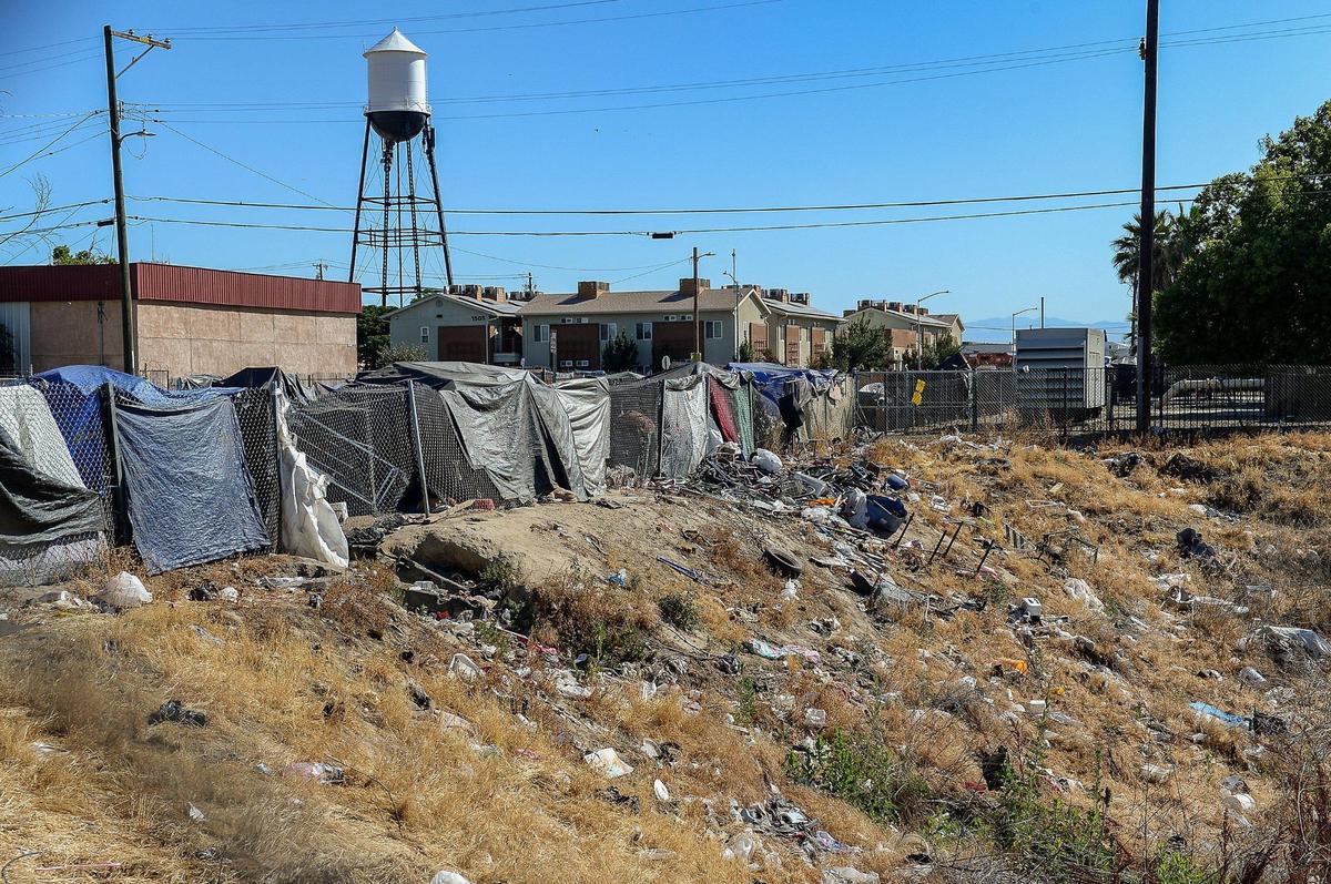 Discarded trash is strewn along the inside of a ponding basin near a homeless encampment in west Fresno on Monday, June 8, 2020. Homelessness has been an issue the west Fresno community has battled for decades.