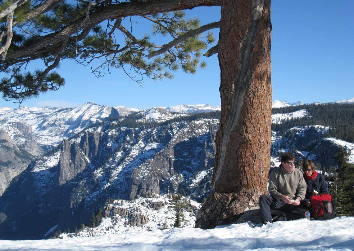 Steve and Margreet Ray of Topanga eat lunch under a stately pine in the snow at Dewey Point after they cross-country skied there from Badger Pass on Jan. 13, 2009. In the background is Yosemite Valley with Half Dome in the distance in the center. 