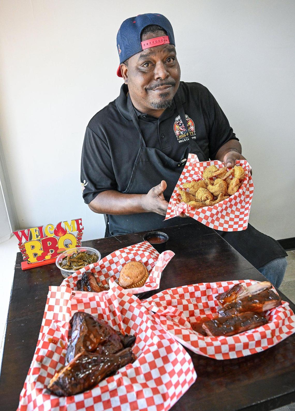 Herman Tatum, owner of Hogg Pitt BBQ & Catering, holds up fried fish and shrimp while sitting with various plates of classic barbecue meats and soul food at his new brick-and-mortar restaurant in Fresno on Monday, June 2, 2025.