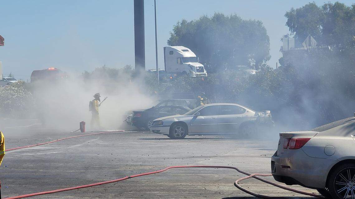 Fire crews work to extinguish a grass fire that spread into the parking lot of a Days Inn, set four vehicles ablaze and left two people hospitalized Sunday, May 30, 2021, in Fresno, California.