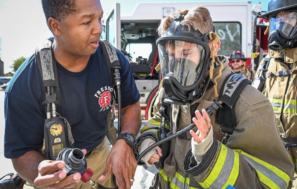 Fresno Fire Captain Will Johnson helps Rusty Davis, 14, of Clovis with his self-contained breathing apparatus during the Fresno Fire Department’s annual “Firefighter for a Day” event where citizens can get an inside look at the job of a firefighter, at the department’s training grounds in Fresno on Saturday, Oct. 22, 2022.